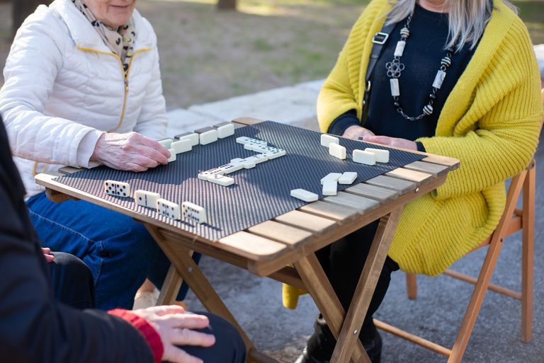 Residents playing dominoes together at a wooden table outdoors