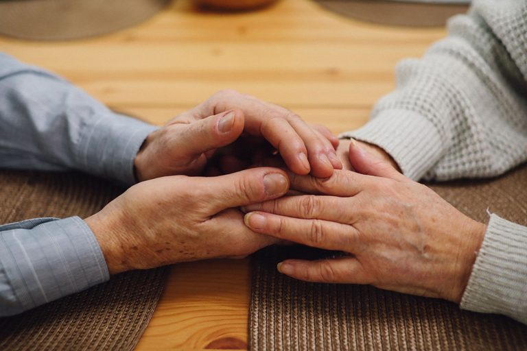 Two pairs of hands held together across a wooden table
