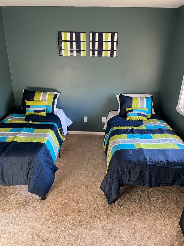 Furnished semi-private bedroom at Heart to Heart Homes with two twin beds in navy and green bedding